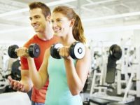 Portrait of handsome coach training woman with dumbbells at gym